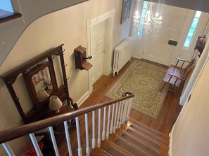 Una escalera con barandilla de madera, una puerta blanca, un radiador y un tapete estampado.