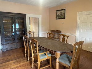 Comedor con una gran mesa de madera rodeada de seis sillas, un aparador de madera oscura con puertas de cristal y paredes de color crema.