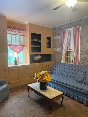 A living room with a blue sofa, a wooden coffee table with a flower vase, and a stone wall.