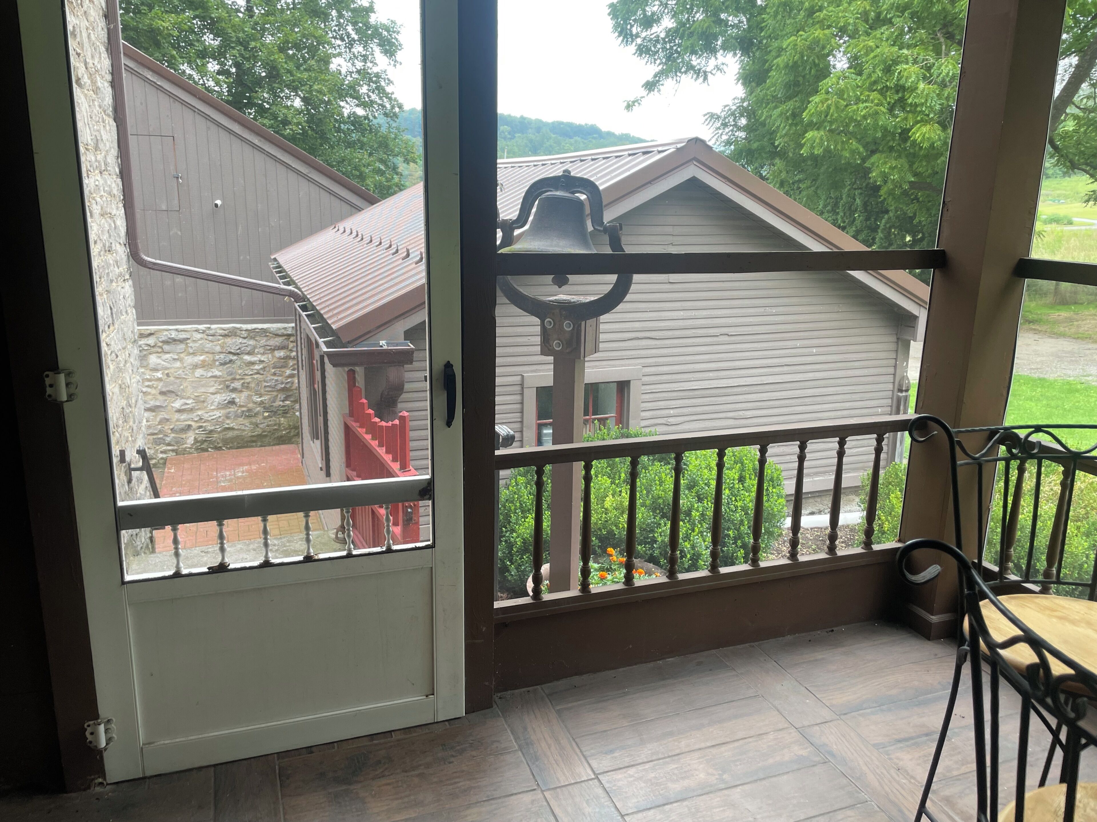 A wooden deck with a metal railing, a stone wall, and a view of a house with a red staircase.