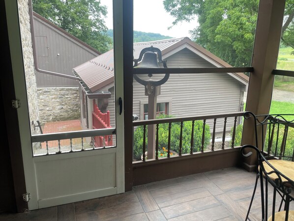 A wooden deck with a metal railing, a stone wall, and a view of a house with a red staircase.