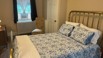 Un dormitorio con cama, una silla, un radiador y una puerta.
