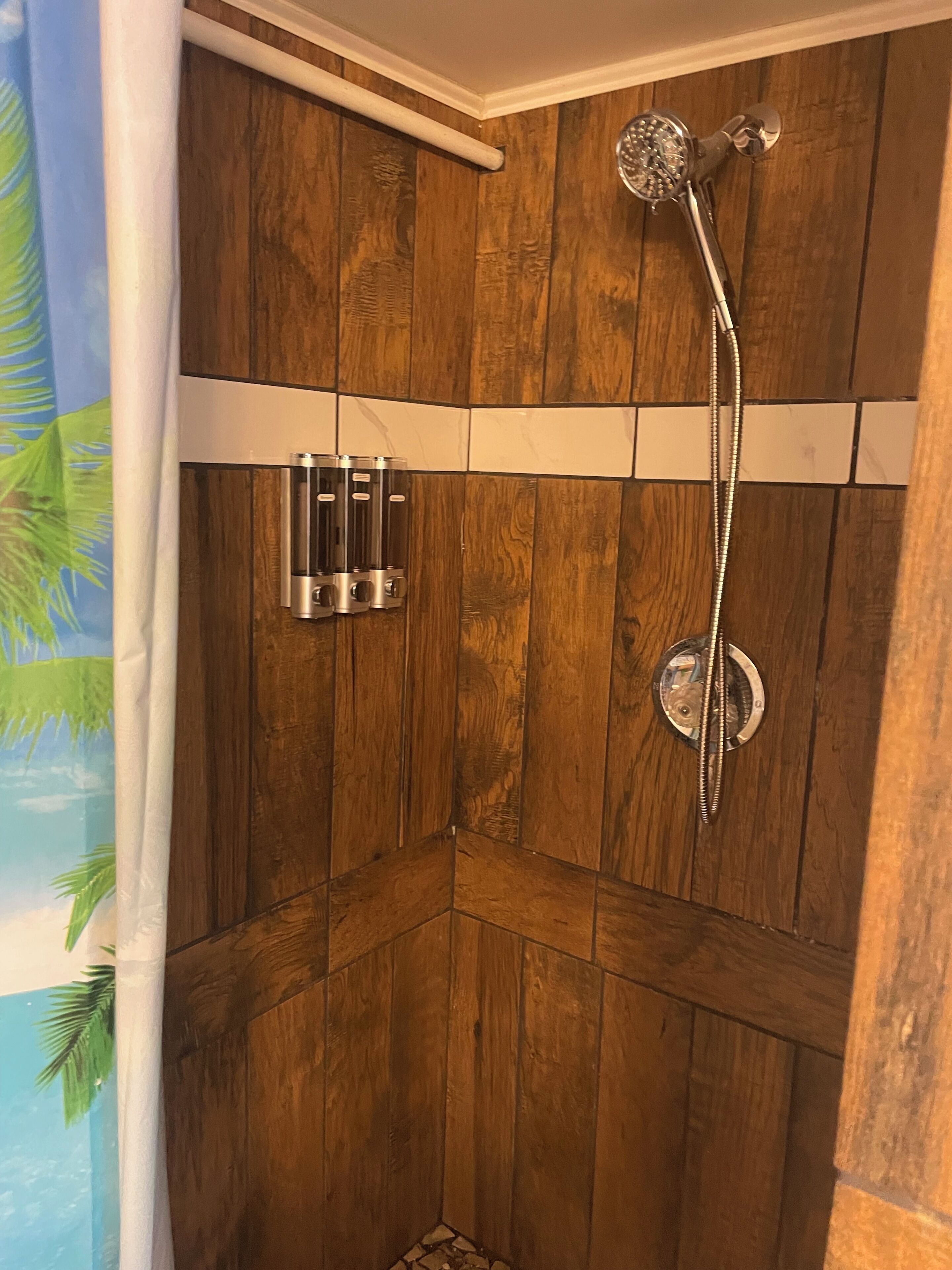 A wooden shower enclosure with a handheld showerhead and a wall-mounted faucet.