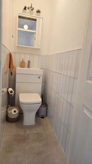 Une petite salle de bain comprenant des toilettes, une poubelle, un porte-serviettes et un miroir au-dessus des toilettes.