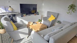 Ein modernes Wohnzimmer mit einer Couch, Sesseln, einem Couchtisch, einem Fernseher, einer Tastatur und Zimmerpflanzen.