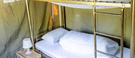 Una cama litera de dos plazas, una mesita de noche pequeña con lámpara, y una cortina en la pared.