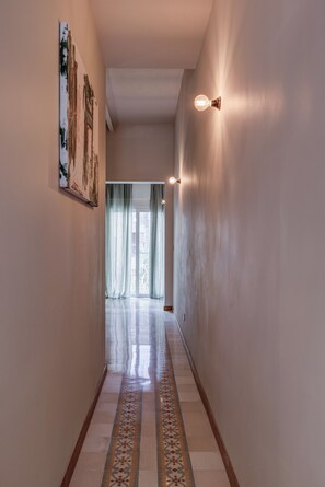 Un couloir avec un revêtement de sol à motifs, un tableau accroché au mur de gauche et un luminaire fixé au mur de droite.