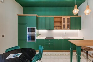 Une cuisine moderne avec des meubles de couleur verte, une table en bois et deux lampes suspendues.
