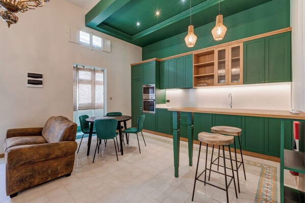 Une cuisine moderne avec des meubles de couleur verte, un plan de travail en bois et deux tabourets de bar.
