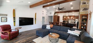 Ein modernes Wohnzimmer mit einem Ecksofa, einem roten Sessel, einem Fernseher und einem Essbereich mit Holztisch und -stühlen.