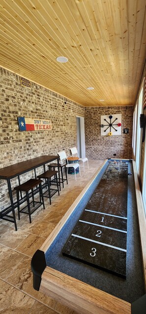 Una stanza con un tavolo da calcio, un lungo tavolo di legno con sedie e una parete in mattoni con una bandiera del Texas.
