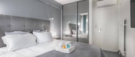 Una habitación de hotel moderna con una cama grande, un armario con espejo y una puerta con unidad de aire acondicionado.