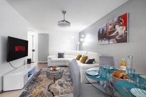 A modern living room with a flat-screen TV, white furniture, a dining area with a table set for two, and a painting on the wall. - Bright One Bedroom Apartment in Cannes - 2394 (Cannes)