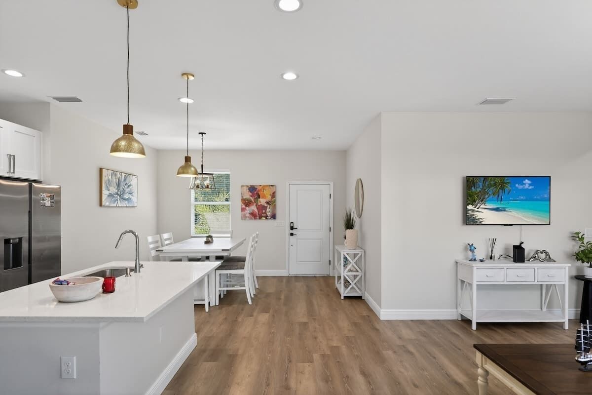 A modern kitchen with white cabinetry, a central island, pendant lighting, and a dining area with chairs.