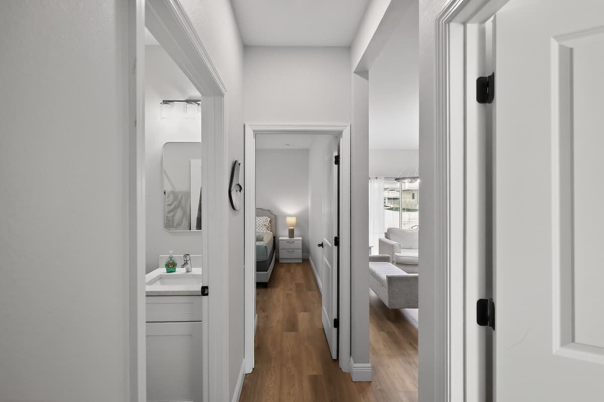 A hallway with a bathroom on the left, a bedroom with a bed and nightstand in the center, and a bathroom with a sink on the right.
