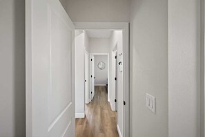 A narrow hallway with white walls and wooden flooring, leading to a door with a circular mirror on the wall. - Beautiful 4/2 Oasis: Beaches Nearby | w/ King Bed (Englewood)