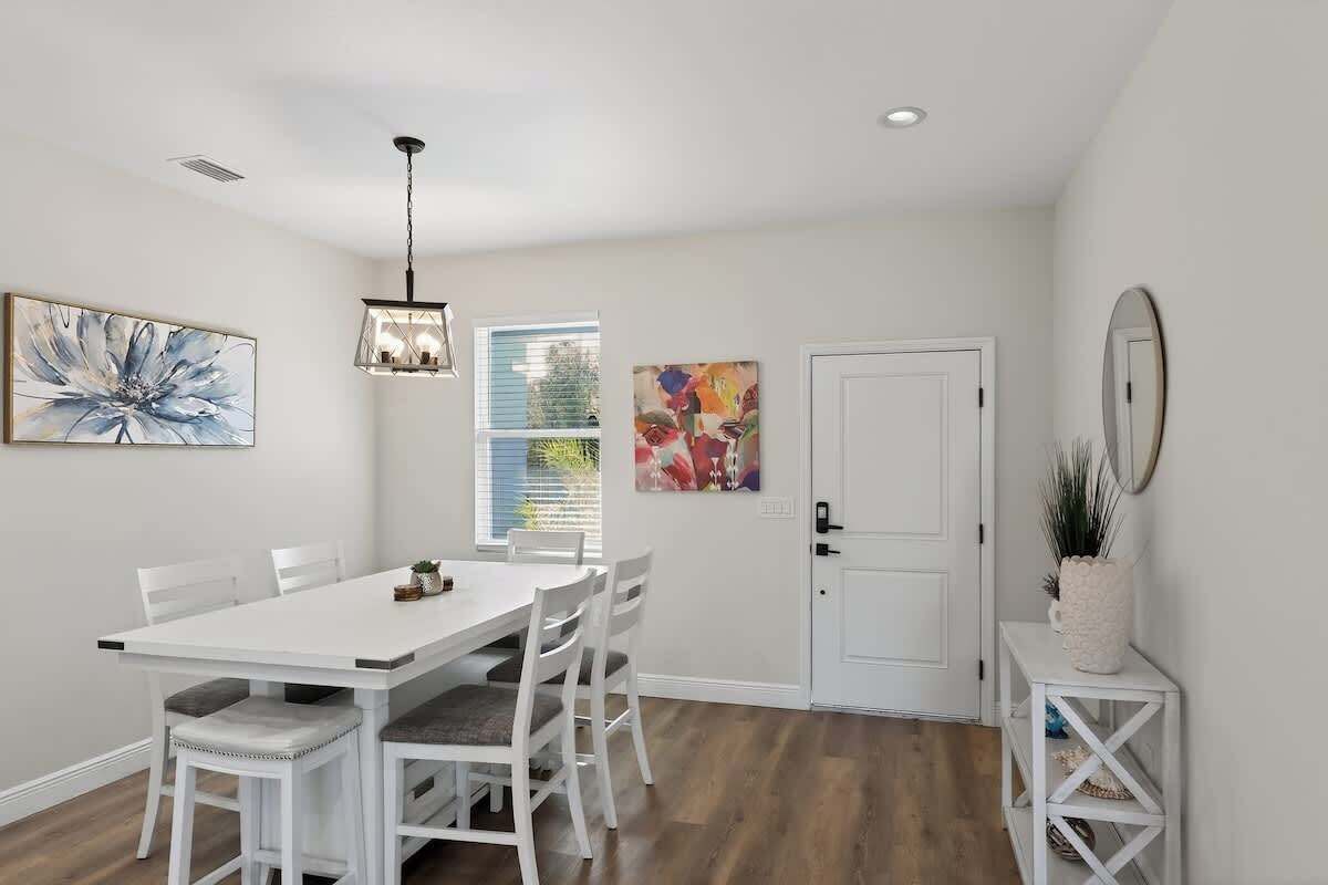 A dining area with a white table and chairs, a pendant light, and artwork on the walls.