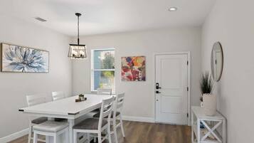 A dining area with a white table and chairs, a pendant light, and artwork on the walls.