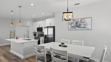 A modern kitchen with white cabinetry, a central island, and a dining area with white chairs.