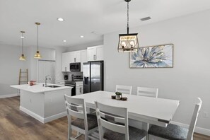 A modern kitchen with white cabinetry, a central island, and a dining area with white chairs. - Beautiful 4/2 Oasis: Beaches Nearby | w/ King Bed (Englewood)