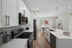 A modern kitchen with stainless steel appliances, white cabinetry, and a central island with a sink.