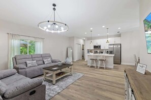 A modern living room with a sofa, coffee table, and a dining area with a kitchen in the background.