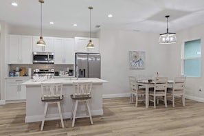 A modern kitchen with white cabinetry, stainless steel appliances, and a central island with bar stools. - Comfortable 4BR Home for Groups (Port Charlotte)