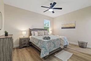 A bedroom with a bed, bedside tables, a ceiling fan, a window, and a wall-mounted artwork.
