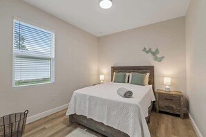 A bedroom with a bed, bedside tables, a window with blinds, and a wall-mounted decoration. - Comfortable 4BR Home for Groups (Port Charlotte)