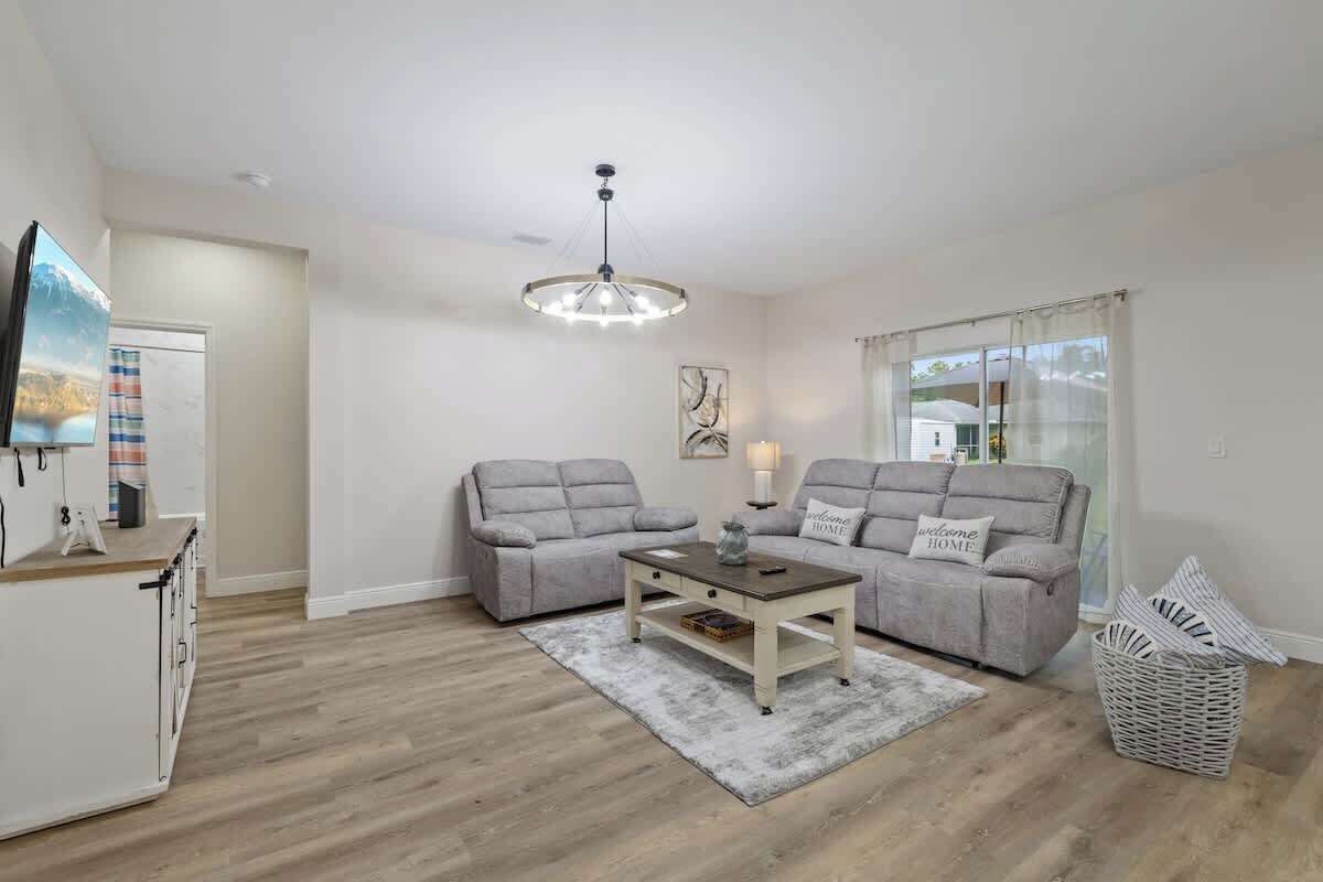 A living room with two grey sofas, a coffee table, a chandelier, and a television on a cabinet.