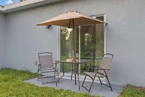 An outdoor patio with a table and chairs, a glass door, and a large umbrella. - Comfortable 4BR Home for Groups (Port Charlotte)