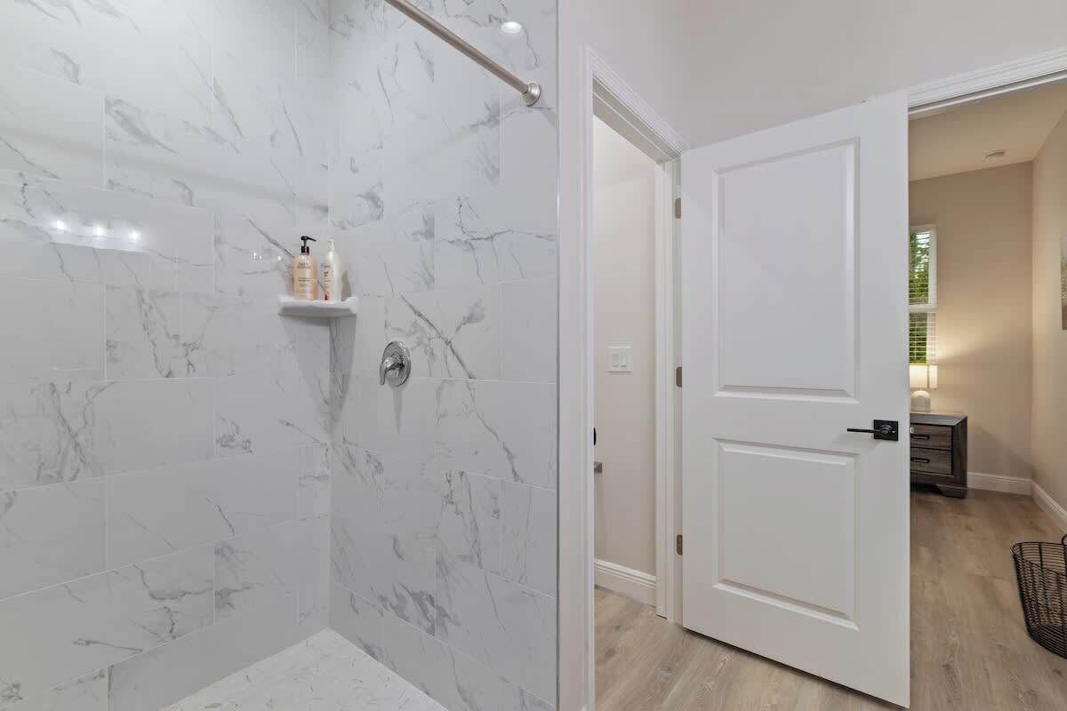 A bathroom with marble tiles, a shower area, and a white door leading to another room.
