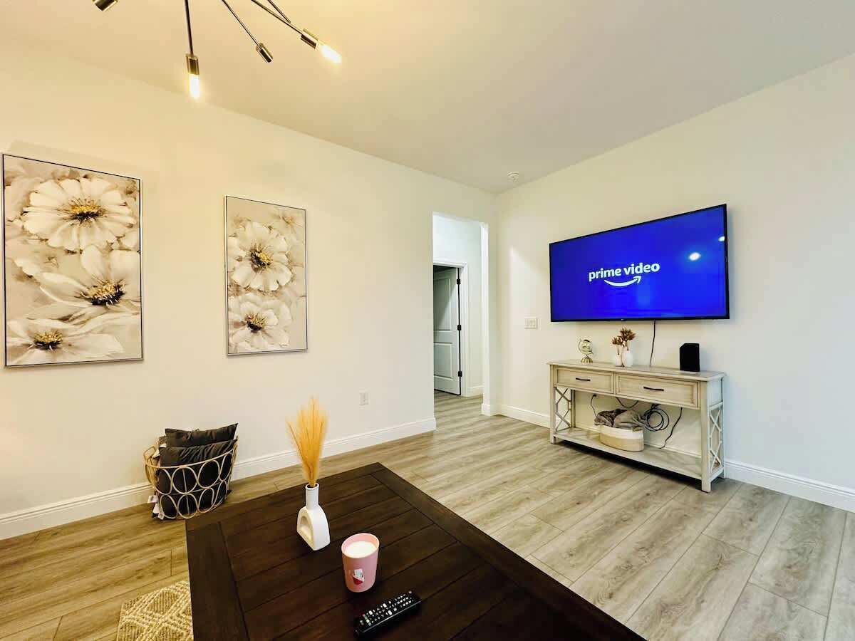 Una sala moderna con televisor de pantalla plana, piso de madera, una mesa de centro con objetos decorativos y un aparador con un altavoz.
