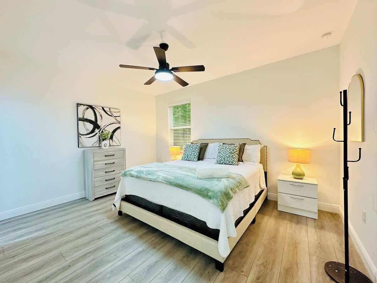 Un dormitorio con cama, ventilador de techo, mesita de noche con lámpara, cómoda y aplique de pared.