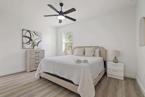 Un dormitorio con cama, mesita de noche, cómoda, ventilador de techo y ventana.
