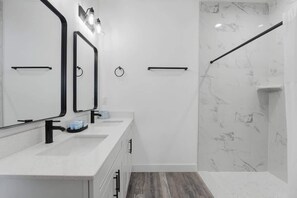 Een moderne badkamer met een witte wastafel, een grote spiegel en een douchegedeelte met marmeren wanden.