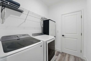 A laundry room with a Samsung washer and dryer, a drying rack, and a white door.