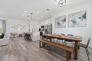Een moderne keuken met witte kasten, roestvrijstalen apparatuur en een houten eettafel met banken.