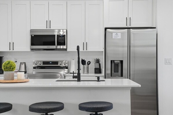 A modern kitchen with white cabinets, stainless steel appliances, a central island with stools, and a built-in water dispenser.