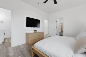 A modern bedroom with a large bed, a flat-screen TV mounted on the wall, and a wooden dresser.