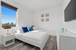 Een moderne slaapkamer met een bed, nachtkastjes, een televisie en een raam met uitzicht.