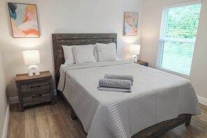 Ein Schlafzimmer mit einem hölzernen Kopfteil, zwei Nachttischen mit Lampen, einem Bett mit weißer Bettwäsche und zwei abstrakten Bildern an den Wänden.