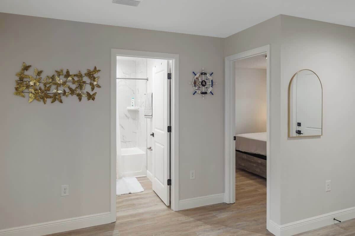 A hallway with a white door leading to a bathroom, a wall-mounted clock, and a decorative leaf arrangement.