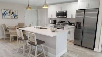 A modern kitchen with white cabinetry, stainless steel appliances, and a central island with bar stools.