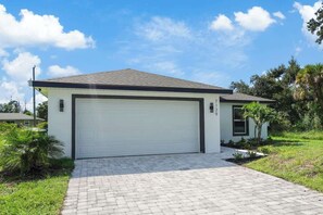 Ein Bungalow mit Garage, befestigter Auffahrt und einem kleinen Rasen mit Palmen.