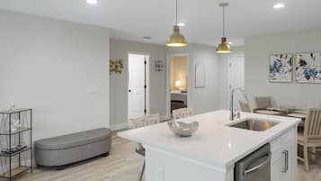 A modern kitchen with a central island, pendant lighting, and a dining area with chairs.