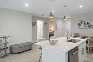 Een moderne keuken met een centraal eiland, hanglampen en een eethoek met stoelen.