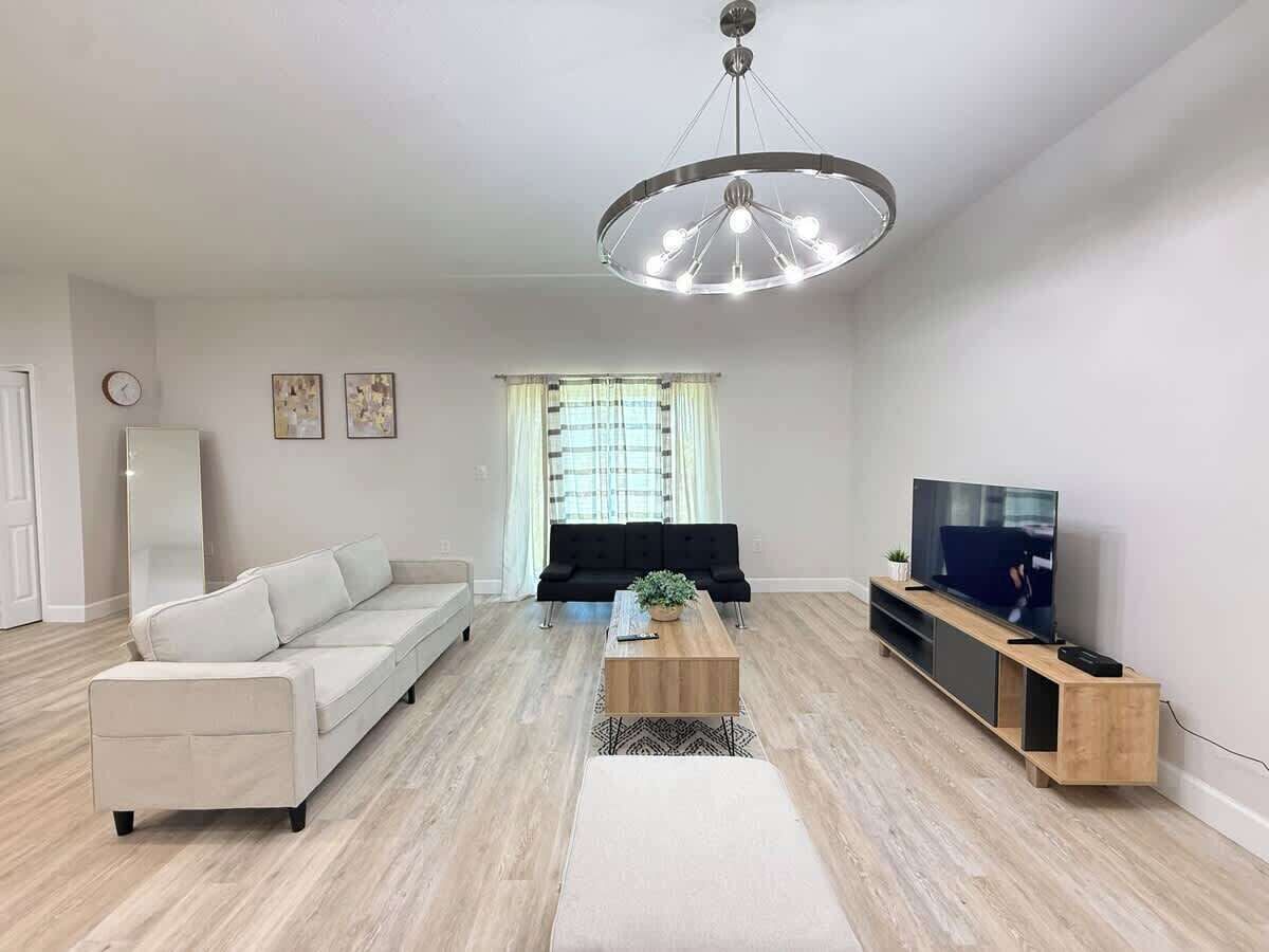 A modern living room with a sofa, coffee table, TV stand, and a chandelier.