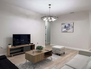 Een moderne woonkamer met een flatscreen televisie, een houten tv-meubel, een salontafel, een grijze bank en een hanglamp.