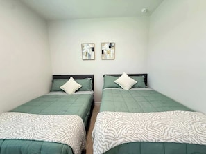 Een kamer met twee bedden, elk met een groene sprei en witte kussens met een patroon. Boven de bedden hangen twee kunstwerken in lijsten.